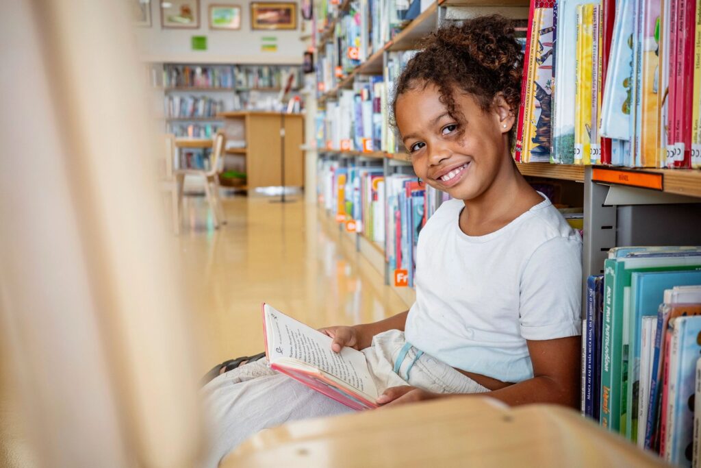 A young girl happily reading a book in a bright library.
