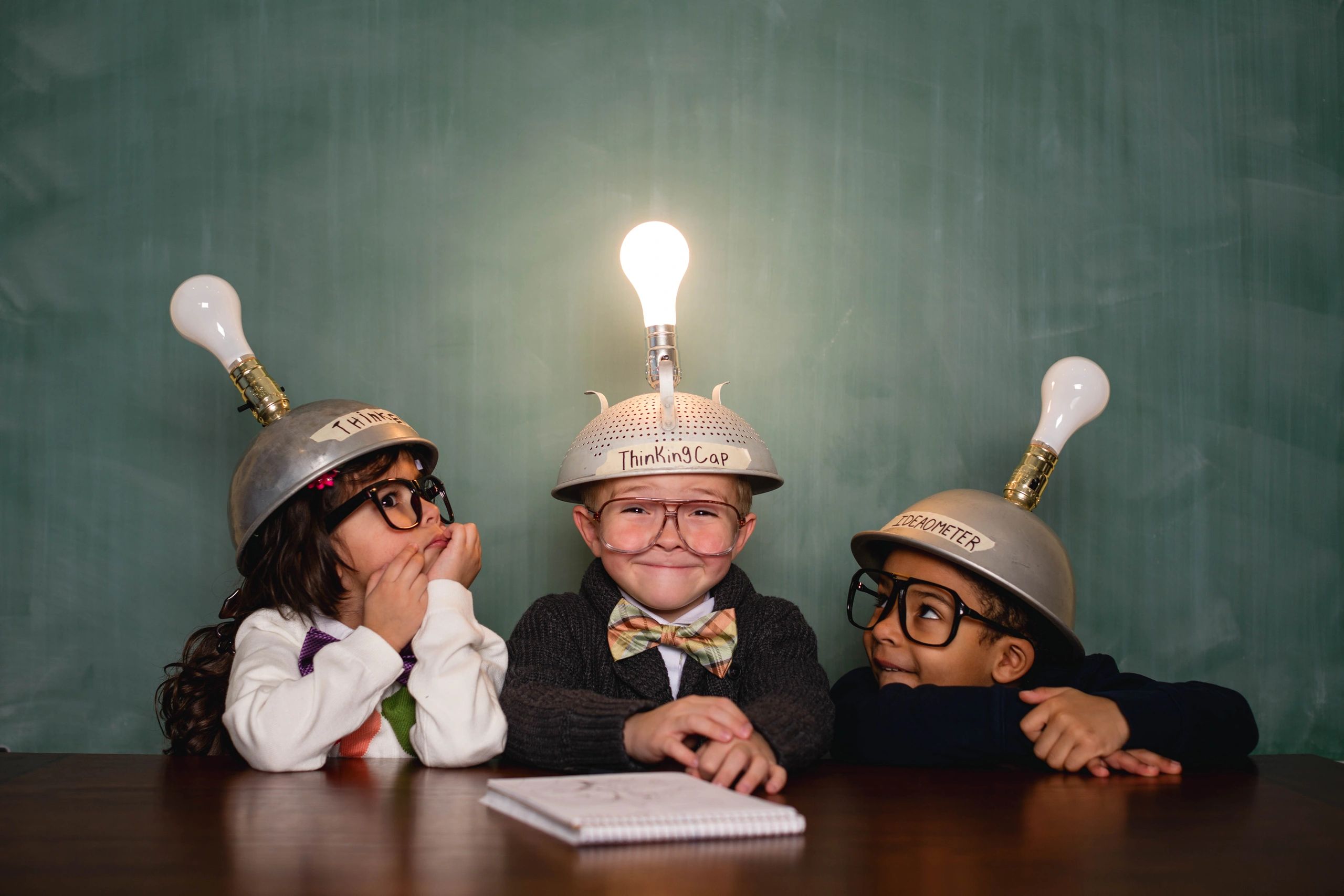 Three children wearing light bulb hats, one with a lit bulb, symbolizing a bright idea.