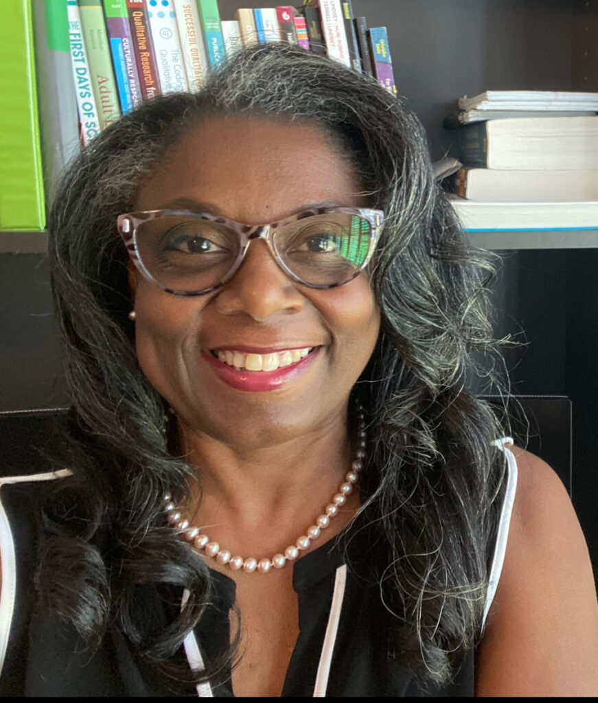 Smiling woman wearing glasses and pearls in a cozy indoor setting.